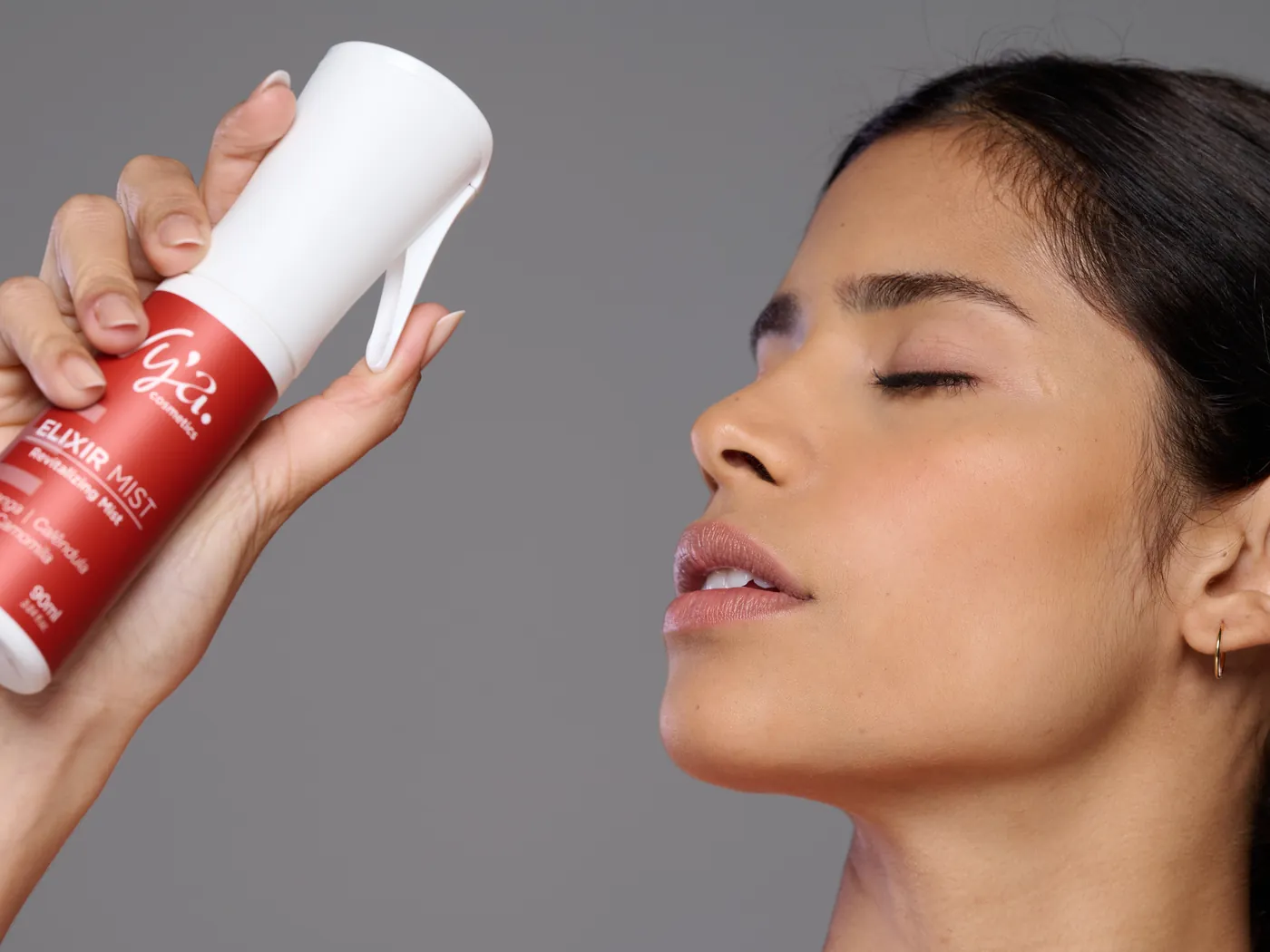 Modelo borrifa o Elixir Mist em direção ao rosto, de olhos fechados. Marcação da névoa e dos 30 cm.