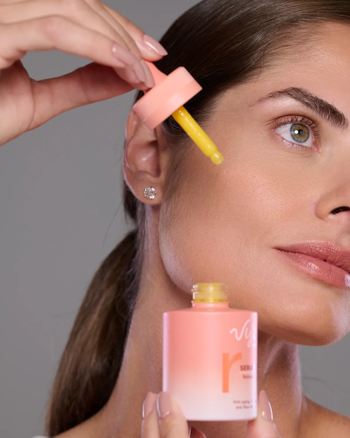 Modelo com a pipeta do Sérum Retinol perto da têmpora. Marcações: da lateral do nariz à têmpora, pela mandíbula e do pescoço para cima; contorno dos olhos excluído.